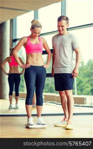 sport, fitness, lifestyle and people concept - smiling man and woman with scales in gym