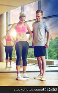sport, fitness, lifestyle and people concept - smiling man and woman with scales in gym. smiling man and woman with scales in gym