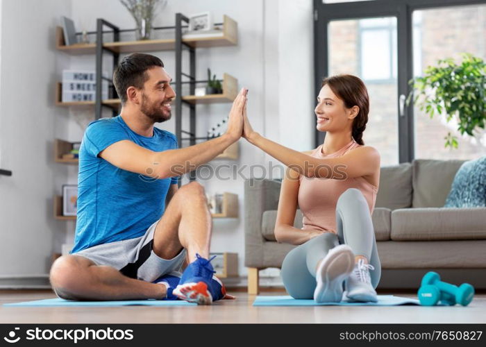 sport, fitness, lifestyle and people concept - smiling man tying laces and woman making high five at home. couple doing sports and making high five at home