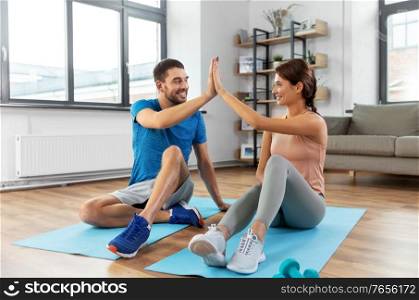 sport, fitness, lifestyle and people concept - smiling man tying laces and woman making high five at home. couple doing sports and making high five at home