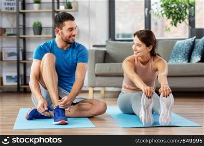sport, fitness, lifestyle and people concept - smiling man tying laces and woman stretching at home. happy couple exercising at home