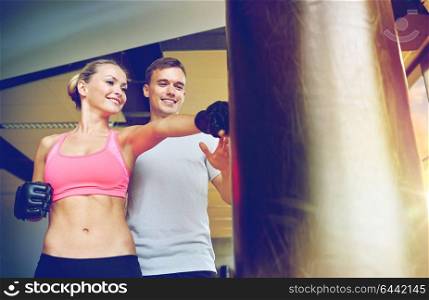 sport, fitness, lifestyle and people concept - smiling woman with personal trainer boxing punching bag in gym. smiling woman with personal trainer boxing in gym