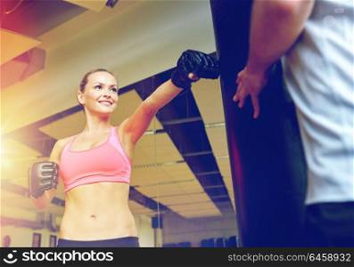 sport, fitness, lifestyle and people concept - smiling woman with personal trainer boxing punching bag in gym. smiling woman with personal trainer boxing in gym