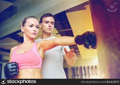 sport, fitness, lifestyle and people concept - woman with personal trainer boxing punching bag in gym. woman with personal trainer boxing in gym