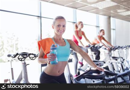 sport, fitness, lifestyle, equipment and people concept - group of women with water bottle riding on exercise bike in gym