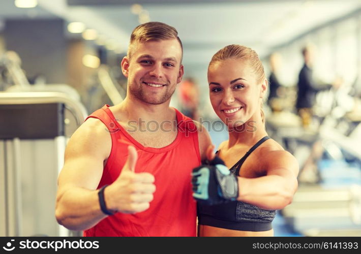 sport, fitness, lifestyle, gesture and people concept - smiling man and woman showing thumbs up in gym