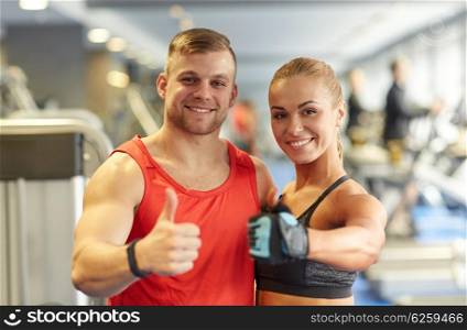 sport, fitness, lifestyle, gesture and people concept - smiling man and woman showing thumbs up in gym