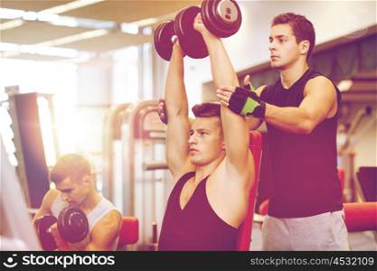 sport, fitness, lifestyle, powerlifting and people concept - group of men with dumbbells and personal trainer flexing muscles in gym
