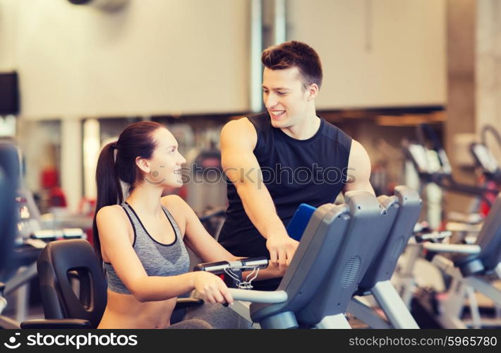 sport, fitness, lifestyle, technology and people concept - happy woman with trainer working out on exercise bike in gym