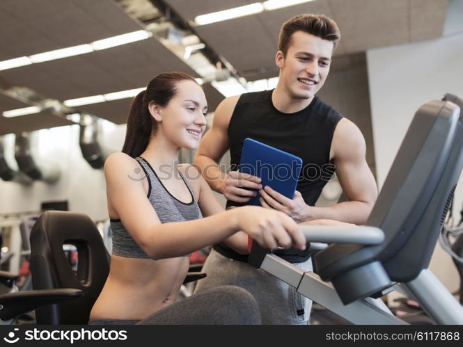 sport, fitness, lifestyle, technology and people concept - happy woman with trainer working out on exercise bike in gym