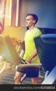 sport, fitness, lifestyle, technology and people concept - man with earphones exercising on treadmill in gym. man with smartphone exercising on treadmill in gym