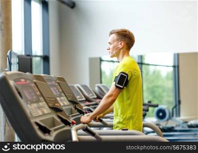 sport, fitness, lifestyle, technology and people concept - man with smartphone and earphones exercising on treadmill in gym