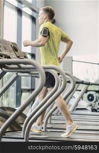 sport, fitness, lifestyle, technology and people concept - man with smartphone and earphones exercising on treadmill in gym