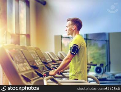 sport, fitness, lifestyle, technology and people concept - man with smartphone and earphones exercising on treadmill in gym. man with smartphone exercising on treadmill in gym