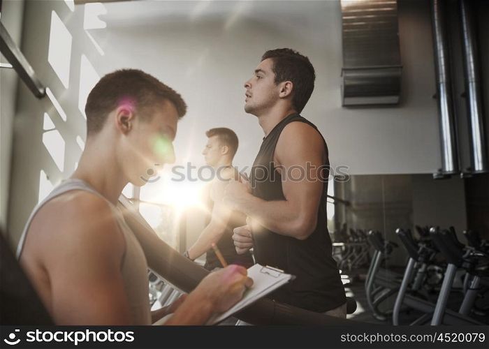 sport, fitness, lifestyle, technology and people concept - men with personal trainer exercising on treadmill in gym