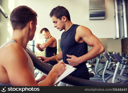 sport, fitness, lifestyle, technology and people concept - men with personal trainer exercising on treadmill in gym