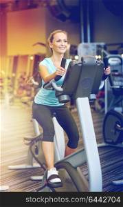sport, fitness, lifestyle, technology and people concept - smiling woman exercising on exercise bike in gym. smiling woman exercising on exercise bike in gym