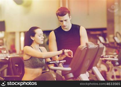 sport, fitness, lifestyle, technology and people concept - woman with trainer working out on exercise bike in gym