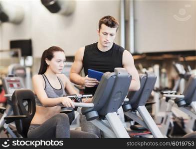 sport, fitness, lifestyle, technology and people concept - woman with trainer working out on exercise bike in gym