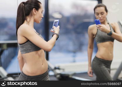 sport, fitness, lifestyle, technology and people concept - young woman with smartphone taking mirror selfie in gym