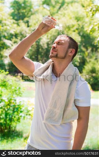 Sport fitness man. Young athletic man cooling himself after training by squirting water over himself from a drinks bottle outdoors at park