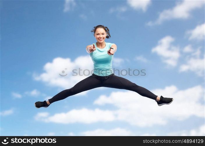 sport, fitness, motion and people concept - happy smiling young woman jumping in air over blue sky and clouds background