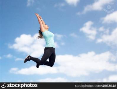sport, fitness, motion and people concept - happy smiling young woman jumping in air or dancing over blue sky background. happy sporty young woman jumping in blue sky