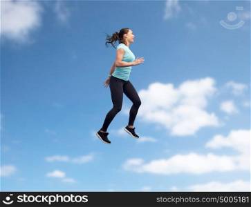 sport, fitness, motion and people concept - happy smiling young woman jumping in air over blue sky background. happy smiling sporty young woman jumping in air