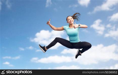 sport, fitness, motion and people concept - happy smiling young woman jumping in air and showing thumbs up over blue sky background. happy sporty young woman jumping in blue sky