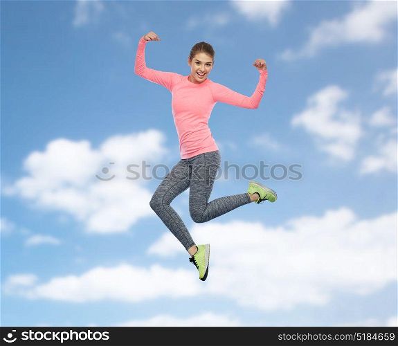 sport, fitness, motion and people concept - happy smiling young woman jumping in air and showing power gesture over blue sky and clouds background. happy smiling sporty young woman jumping in sky