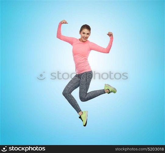 sport, fitness, motion and people concept - happy smiling young woman jumping in air and showing power gesture over blue background. happy smiling sporty young woman jumping in air