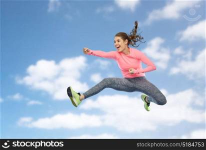 sport, fitness, motion and people concept - happy young woman jumping in air in fighting pose over blue sky and clouds background. happy sporty young woman jumping in fighting pose