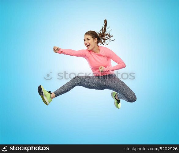 sport, fitness, motion and people concept - happy young woman jumping in air in fighting pose over blue background. happy sporty young woman jumping in fighting pose