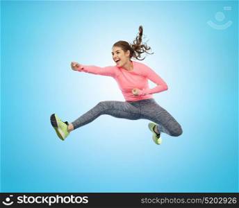 sport, fitness, motion and people concept - happy young woman jumping in air in fighting pose over blue background. happy sporty young woman jumping in fighting pose
