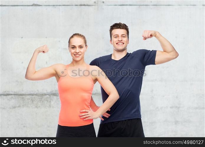 sport, fitness, power, strength and people concept - happy sportive man and woman showing biceps over concrete wall background. happy sportive man and woman showing biceps power