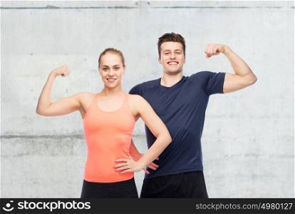 sport, fitness, power, strength and people concept - happy sportive man and woman showing biceps over concrete wall background. happy sportive man and woman showing biceps power