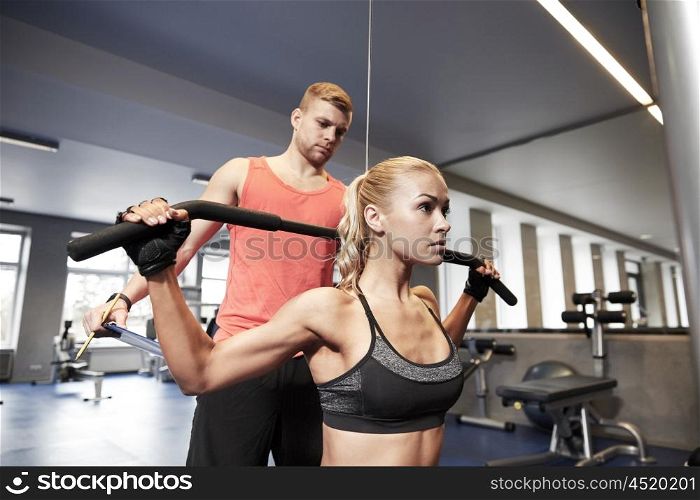 sport, fitness, teamwork and people concept - young woman and personal trainer flexing muscles on cable gym machine