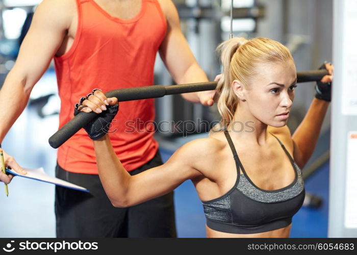 sport, fitness, teamwork and people concept - young woman and personal trainer flexing muscles on gym machine