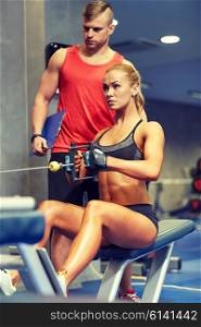 sport, fitness, teamwork and people concept - young woman and personal trainer flexing muscles on gym machine