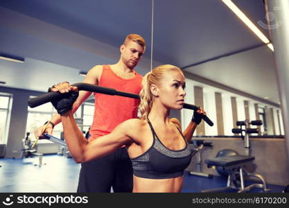 sport, fitness, teamwork and people concept - young woman and personal trainer flexing muscles on cable gym machine