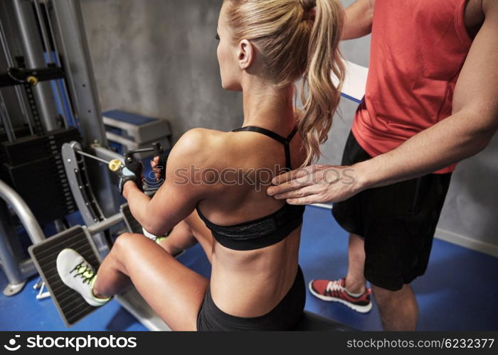 sport, fitness, teamwork and people concept - young woman and personal trainer flexing muscles on cable gym machine