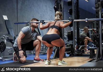 sport, fitness, teamwork, bodybuilding and people concept - young woman and personal trainer with barbell bar flexing muscles in gym