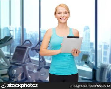 sport, fitness, technology, advertisement and people concept - smiling sporty woman with tablet pc computer over gym machines background