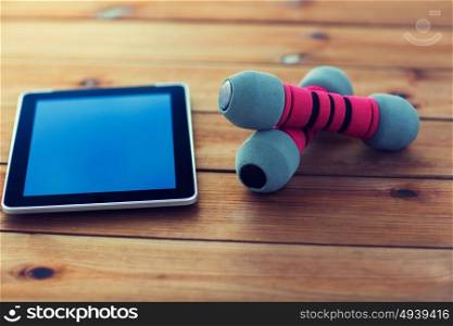 sport, fitness, technology and objects concept - close up of dumbbells and tablet pc computer on wooden floor. close up of dumbbells and tablet pc on wood