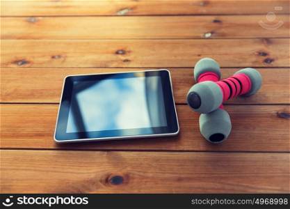 sport, fitness, technology and objects concept - close up of dumbbells and tablet pc computer on wooden floor. close up of dumbbells and tablet pc on wood