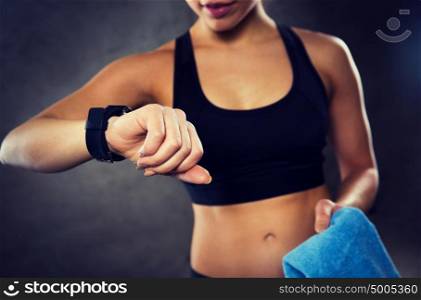 sport, fitness, technology and people concept - close up of young woman with heart-rate or smart watch and towel in gym. close up of woman with smartwatch and towel in gym