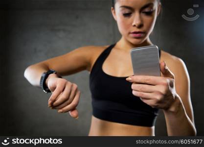 sport, fitness, technology and people concept - close up of young woman with heart-rate or smart watch and smartphone in gym