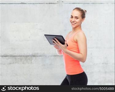 sport, fitness, technology and people concept - happy smiling sportive young woman with tablet pc computer over concrete wall background. happy smiling sportive young woman with tablet pc