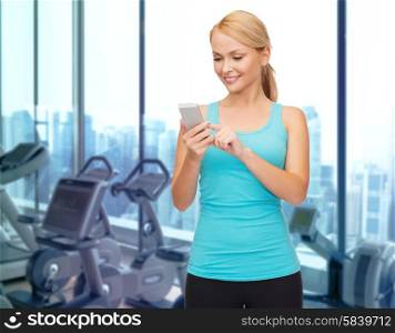 sport, fitness, technology and people concept - smiling sporty woman texting message on smartphone over gym machines background