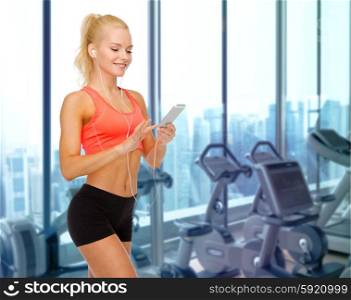 sport, fitness, technology and people concept - smiling sporty woman with smartphone and earphones listening to music over gym machines background